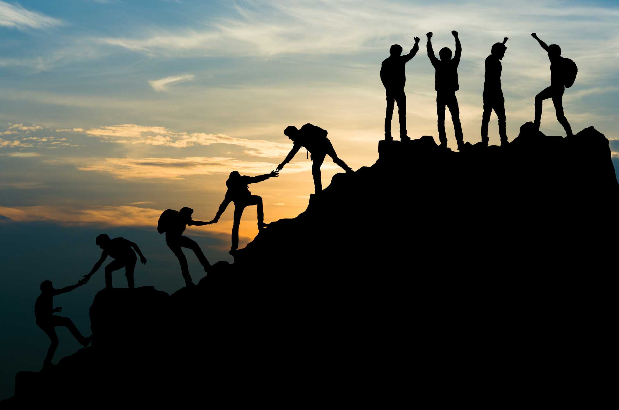 Group of people helping each other climb a mountain
